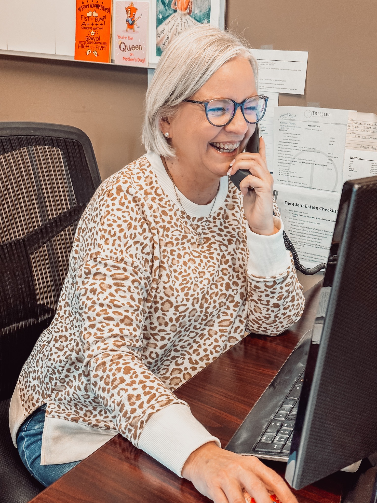 Lisa Chaney smiling while talking on the phone with a client at her desk on the computer