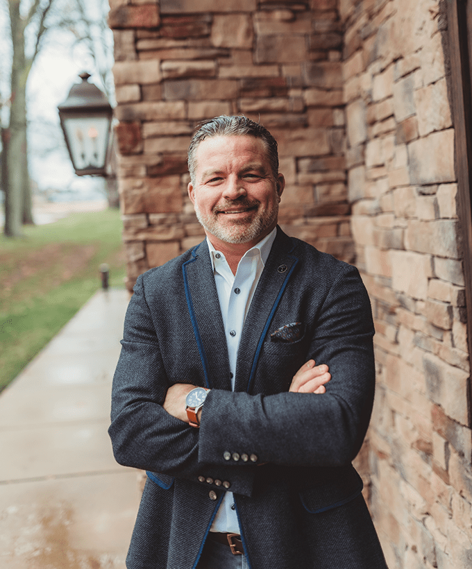 Attorney, Founder and CEO Todd A. Tressler, II in a navy blazer standing outside in front of stone entrance to office