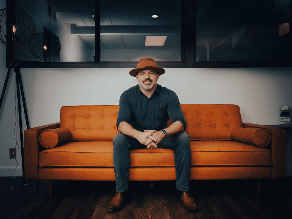 Todd Tressler in a hat sitting on a leather couch